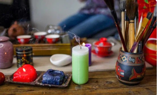 Green extinguished candle with smoke, paintbrushes in decorated pot, red and blue candles on wooden table