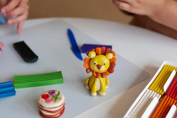 Close-up of colorful modeling clay lion sculpture and craft tools on a white table with kids' hands