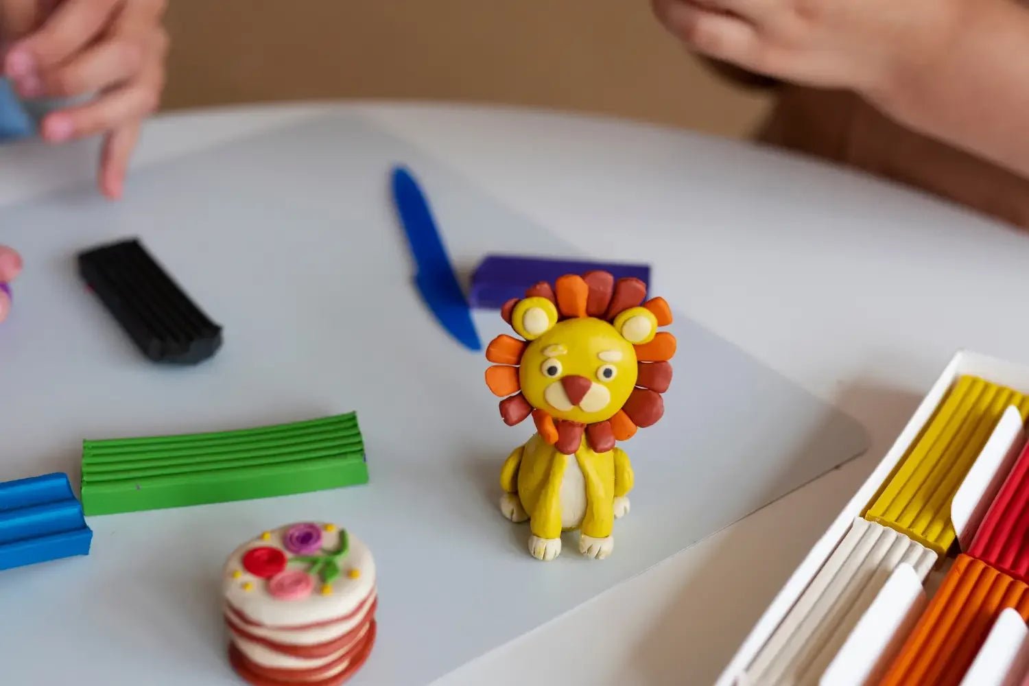 Close-up of colorful modeling clay lion sculpture and craft tools on a white table with kids' hands