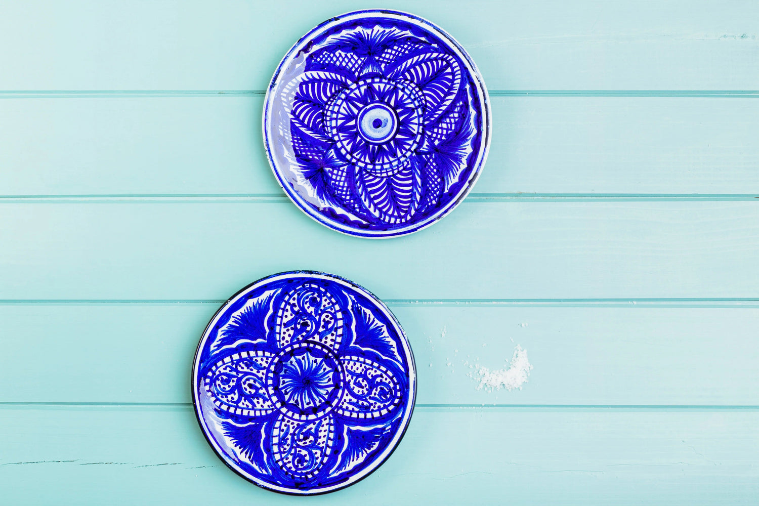 Two handmade ceramic plates with blue intricate patterns on a light blue wooden background