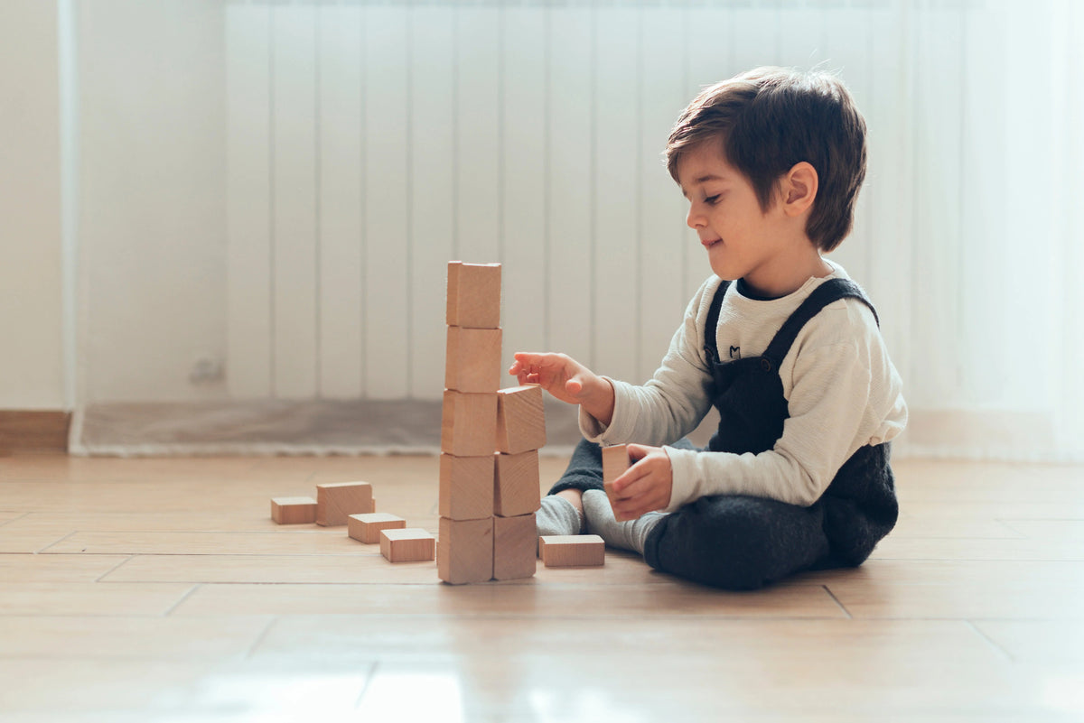 Young boy playing with wooden blocks on a light wooden floor in a bright home