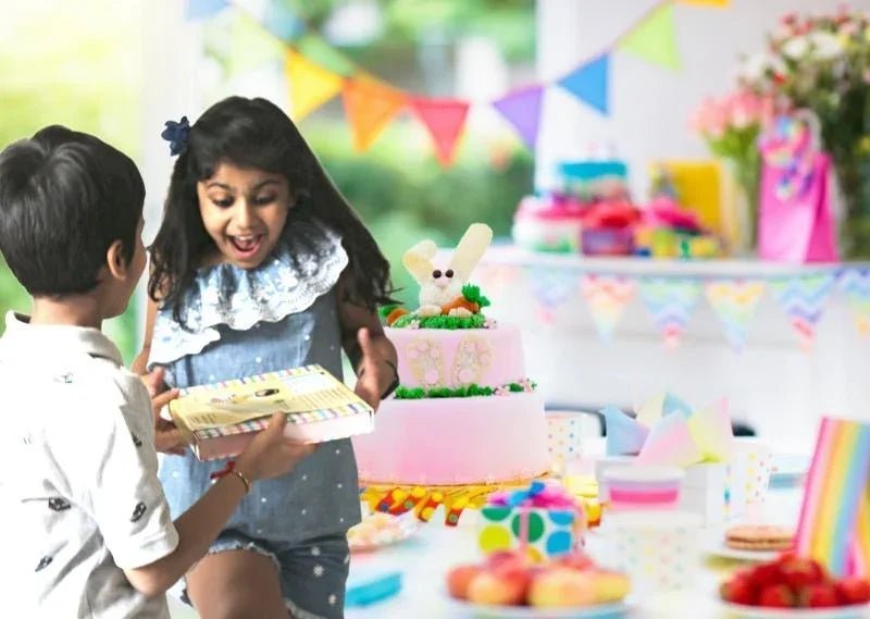 Excited girl receiving a birthday gift from boy at colorful birthday party with pink cake and decorations