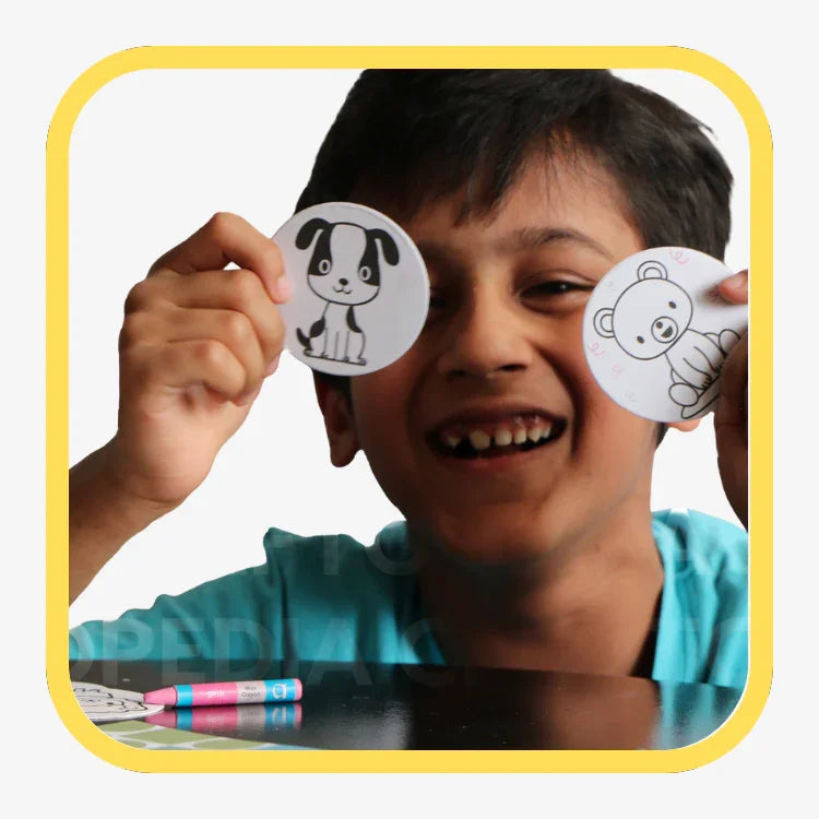 Smiling child holding round cards with black-and-white dog and bear illustrations, colorful markers on table