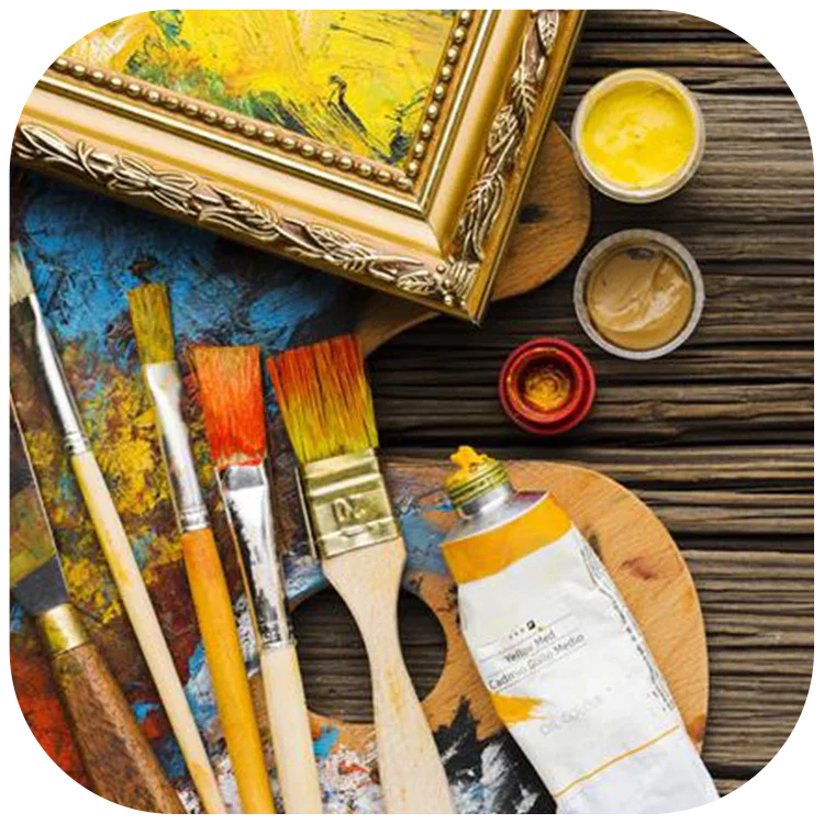 Assorted paintbrushes, yellow paint tube, open paint jars, and framed artwork on wooden surface