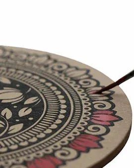 Close-up of a hand painting red petals on a black and natural wood circular folk art lotus tealight holder